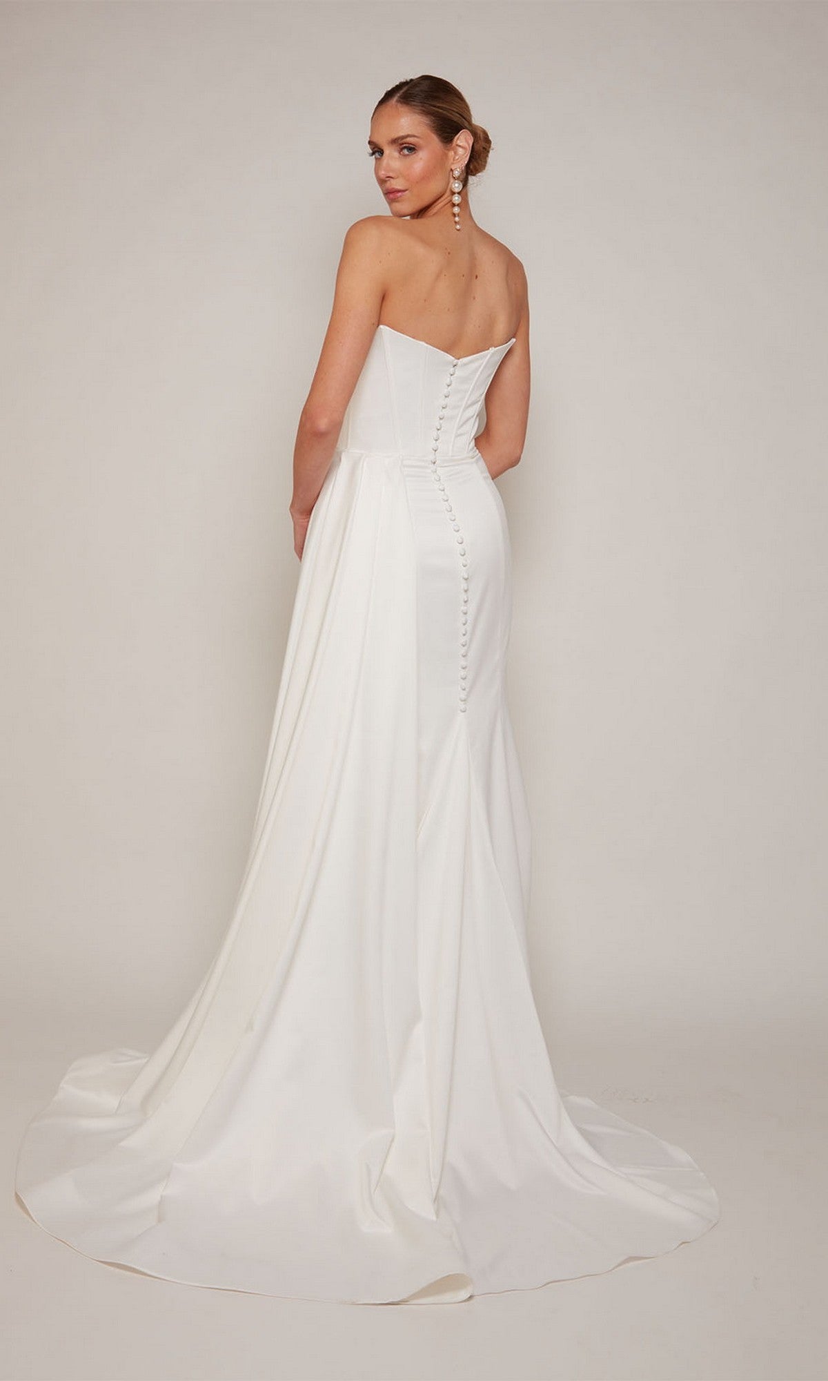 A woman models the Alyce 7093 long formal dress, featuring a strapless satin design with a fitted bodice, buttoned back, thigh-high slit, and long train, standing against a plain light backdrop.